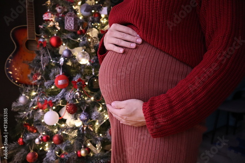 Pregnant woman holding her belly on the background of Christmas tree