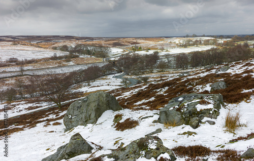 North York Moors with large boulders, trees, rolling landscape under cloudy sky after snow. Goathland, UK.