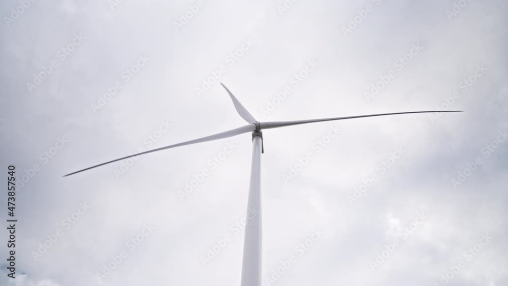 Turning blades at full speed on large farm in offshore or field. Rotating windmill on grey sky background. Clean renewable energy producing by wind turbines. Alternative lifestyle Turning blades at full speed on large farm in offshore or field. Rotating windmill on grey sky background. Clean renewable energy producing by wind turbines. Alternative lifestyle