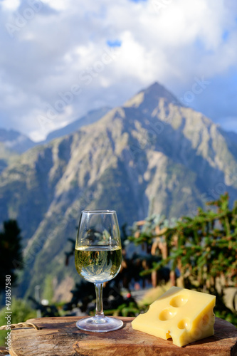 Glass of swiss or savoy dry white wine and yellow emmental cheese with Alpine mountains peaks on background