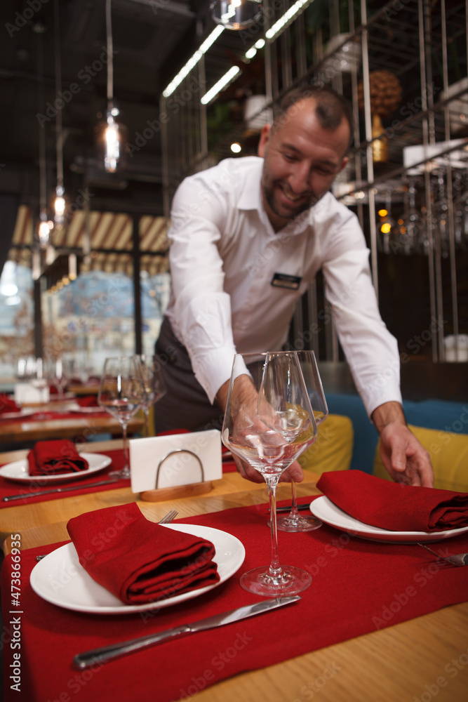 Vertical shot of a cheerful waiter enjoying preparing tables for restaurant guests