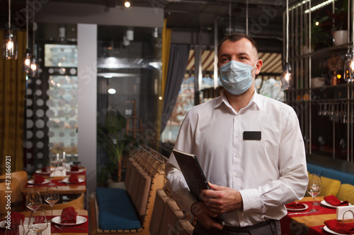 Waiter wearing medical face mask, carrying menu, working at restaurant during quarantine