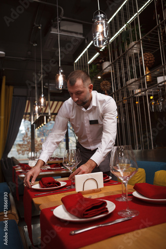 Foto Vertical portrait of a male waiter preparing tables for customers at the restaur
