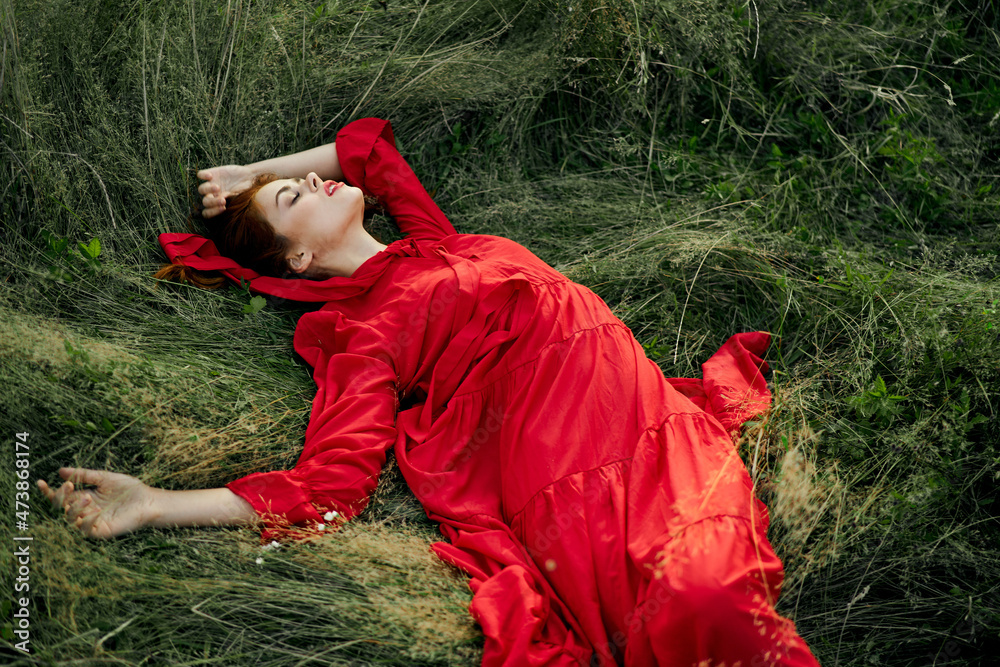 woman in red dress lies on the grass in the field nature landscape woman in red dress lies on the grass in the field nature landscape