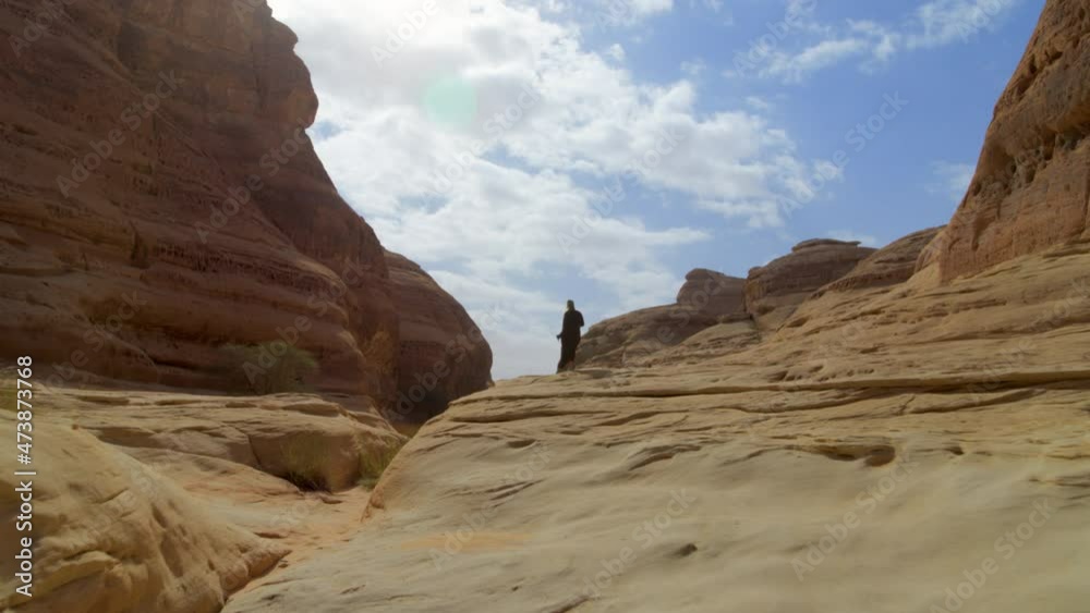 Aerial Panning A Woman Climbing A Large Desert Rock Formation And Ancient Tombs On A Bright Sunny Day - Hegra, Saudi Arabia Aerial Panning A Woman Climbing A Large Desert Rock Formation And Ancient Tombs On A Bright Sunny Day - Hegra, Saudi Arabia