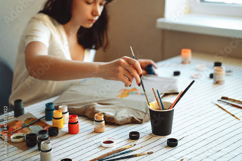 A young woman draws on fabric, on a T-shirt drawing with acrylic paints.
