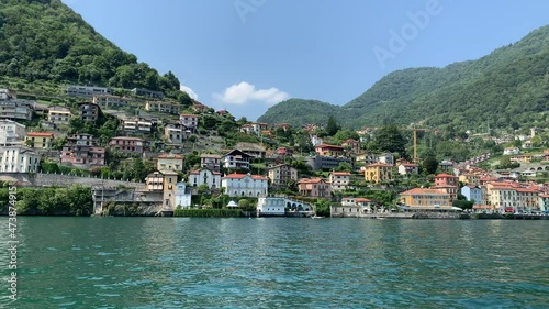 Skyline of Argegno town with houses on hills, mountains. Landscape of Como Lake (Lago di Como) shore. View from the moving boat. Motion of waves and emerald water. Argegno, Como Lake, Lombardy, Italy. photo