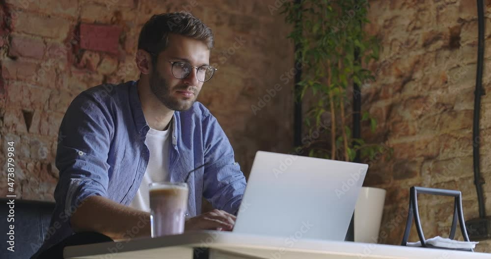 A middle view of thoughtful serious man in eyeglass sit with laptop thinking of solution at cafe. Slow motion A middle view of thoughtful serious man in eyeglass sit with laptop thinking of solution at cafe. Slow motion