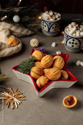 Homemade cookies, nuts stuffed in a bowl in the form of a star, cups with cocoa, a blanket and fir branches. Close-up, vertical