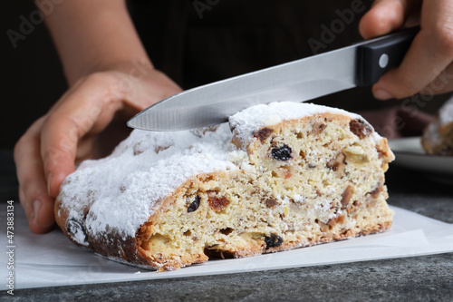 Woman cutting traditional Christmas Stollen at grey table, closeup