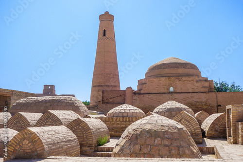 Minaret and madrasah of Bikadjon-Bika, Khiva, Uzbekistan. Building was built by khan's sister named Bikadjan in 1894. Landmark of Dishan-Kala (outer city). Foreground: traditional ancient burials
