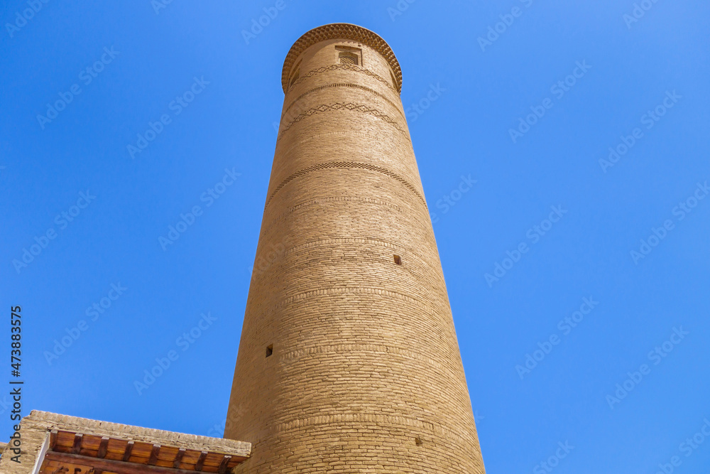 Minaret of Palvan-Kari Madrasah on blue sky background. Tower is interesting in that it does not taper towards top, unlike others. Landmark of historical 