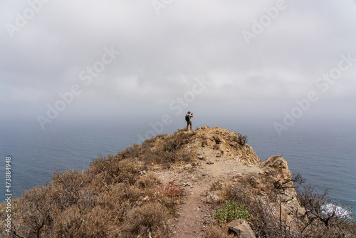 A lone tourist photographer stands on a mountain, against the backdrop of the ocean. Tenerife. Canary Islands. Spain.