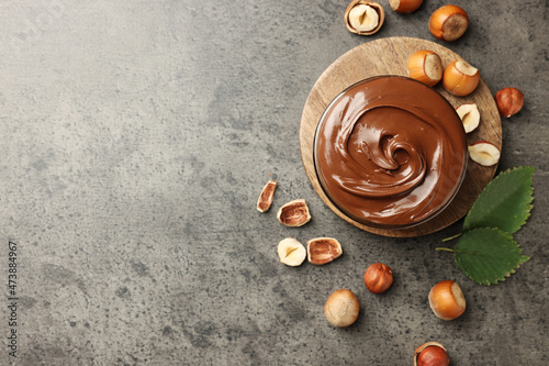 Tasty chocolate hazelnut spread and nuts on grey table, flat lay. Space for text