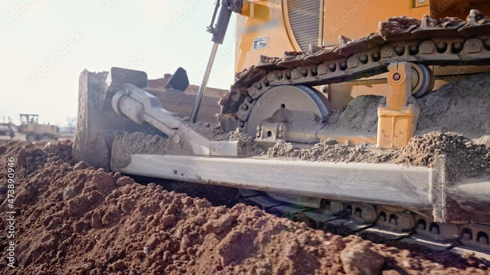 Tracking shot of crawler bulldozer working on construction site or quarry. Mining machinery moving clay, smoothing gravel surface for new road. Earthmoving, excavations, digging on soils.