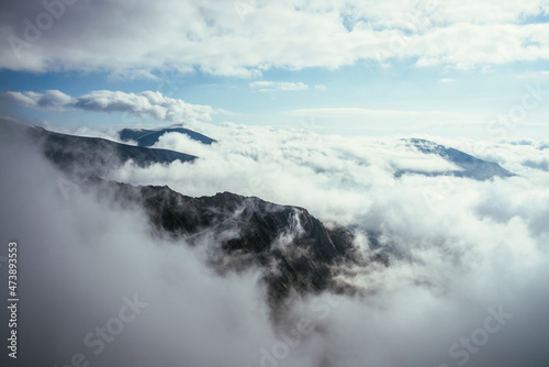 Wonderful alpine scenery with great rocks and mountains in dense low clouds. Atmospheric highlands landscape with mountain tops above clouds. Beautiful view to snow mountain peaks over thick clouds. © Daniil