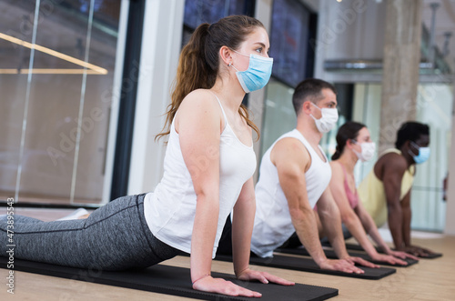 Portrait of young woman in face mask making pilates exercises with group in yoga studio during coronavirus pandemic