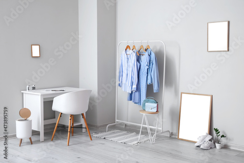 Interior of light room with modern workplace, clothes and blank frames © Pixel-Shot