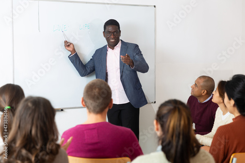Friendly male teacher lecturing to adult students at auditorium