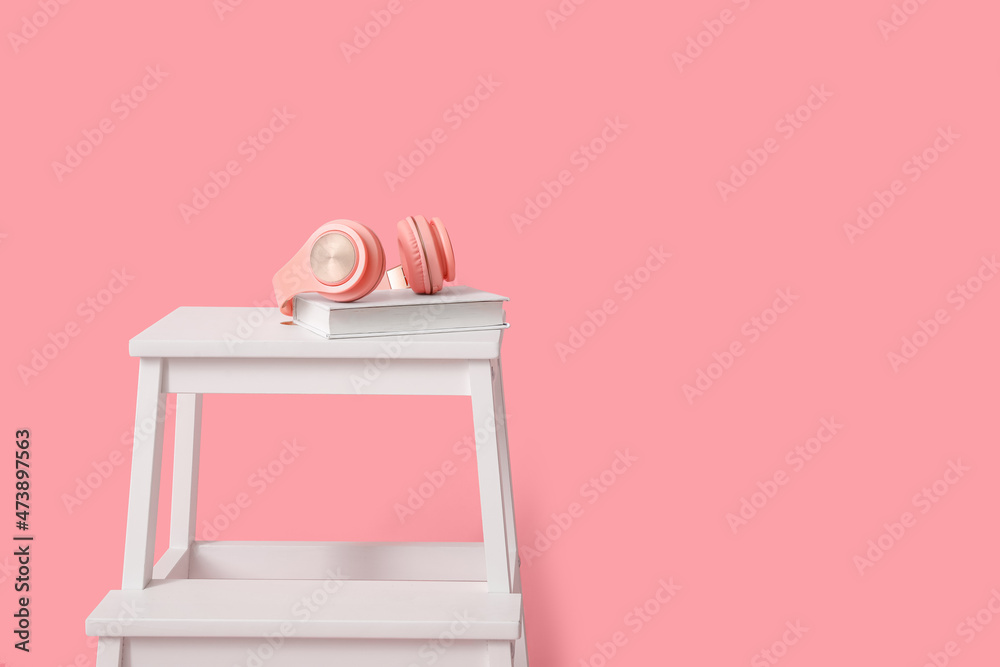 White step stool with headphones and books on pink background White step stool with headphones and books on pink background