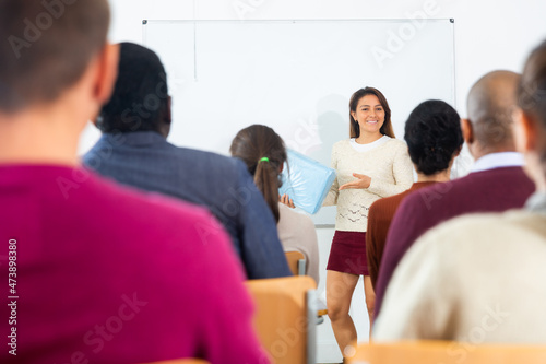 Latina coach businesswoman giving talk at modern office conference to multiethnic team in front of whiteboard