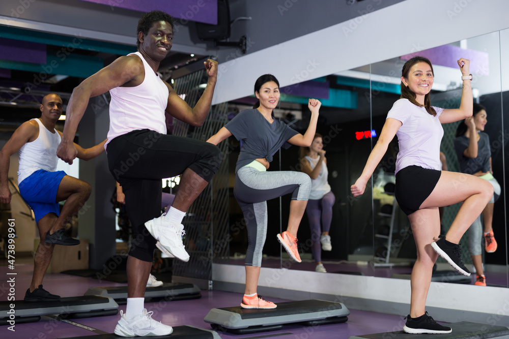 Group of sporty people working out with steppers in fitness center