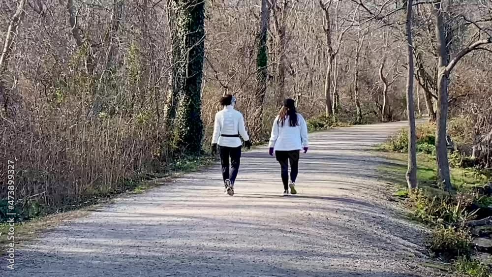Two women walking together on a dirt path in the woods on a early ...