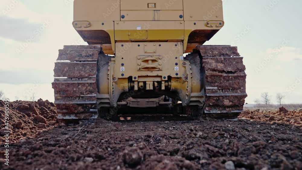 Tracking shot of crawler bulldozer working on construction site or quarry. Mining machinery moving clay, smoothing gravel surface for new road. Earthmoving, excavations, digging on soils.