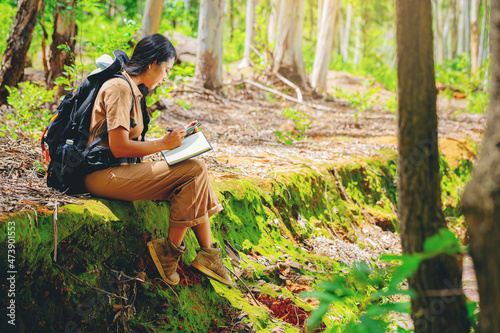 Biologist or botanist recording information about small tropical plants in forest. The concept of hiking to study and research botanical gardens by searching for information.