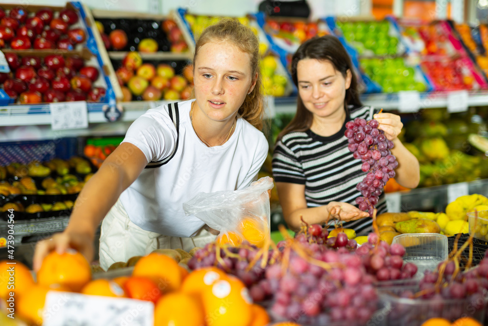 Portrait of teenage girl and her mother who buying fresh red grape at grocery shop