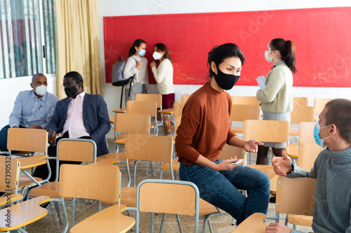Students in protective masks are talking about homework at the desk
