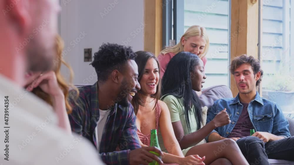 Multi-cultural group of friends sitting on sofas at home together enjoying drinks and talking - shot in slow motion