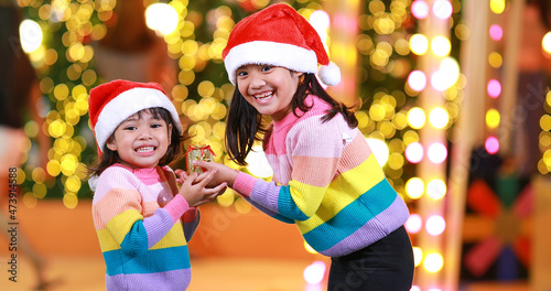 New year anticipation.Two cute little girl Wearing a red Christmas hat and beautiful color shirt on a christmas background with bokeh lights .Have fun and have fun during this important season.
