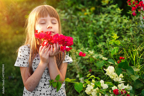 Little girl smelling colorful flowers at summer day in the yard