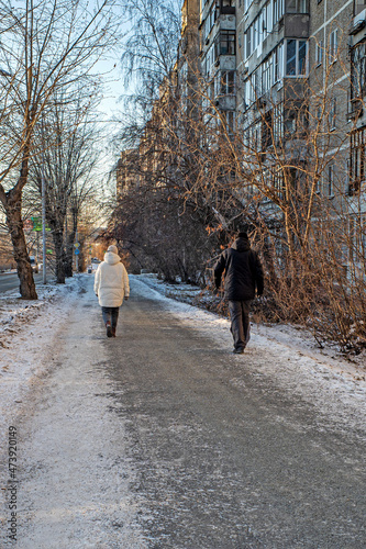 A man and a woman walk along a snowy sidewalk on a winter day © vladimir subbotin