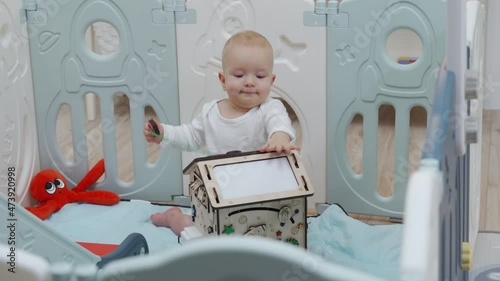 Cute baby boy playing with wooden busy board on montessori busy house. Educational toys. 8 month old baby boy wearing safety helmet enjoy playing time in baby playpen. High quality 4k footage photo