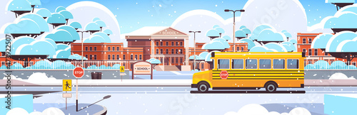 snowy school building empty front yard with trees road and school buswinter cityscape background