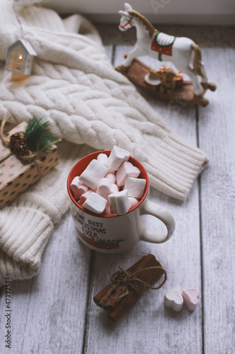 A mug with marshmallows, a white sweater, toys on a light photo background.