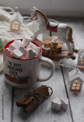 A mug with marshmallows, a white sweater, toys on a light photo background.