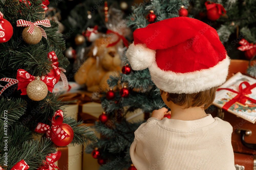 A child with Santa Clause hat helps to decorate Christmas tree
