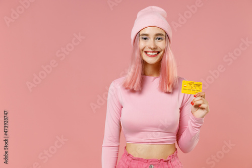 Young smiling woman 20s with bright dyed rose hair in rosy top shirt hat hold in hand credit bank card isolated on plain light pastel pink background studio portrait. People lifestyle fashion concept.