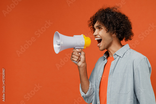 Young student black man 50s wearing blue shirt t-shirt hold scream in megaphone announces discounts sale Hurry up isolated on plain orange color background studio portrait. People lifestyle concept.