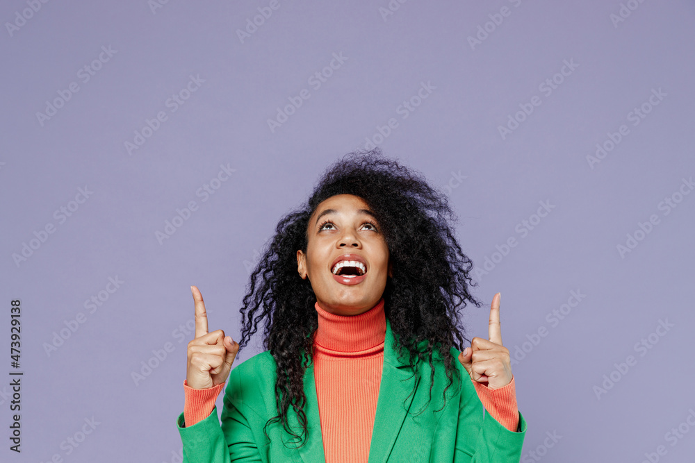 Promoter excited happy young black curly woman 20s years old wears green shirt pointing up above on workspace area copy space mock up isolated on plain pastel light violet background studio portrait.