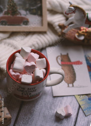 A mug with marshmallows, a white sweater, toys on a light photo background.