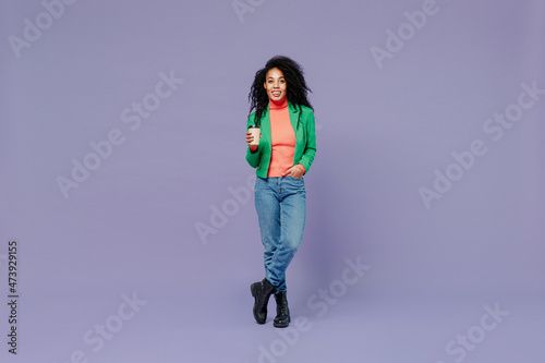 Full size body length happy young black curly woman 20s wears casual clothes hold takeaway delivery craft paper brown cup coffee to go isolated on plain pastel light violet background studio portrait.