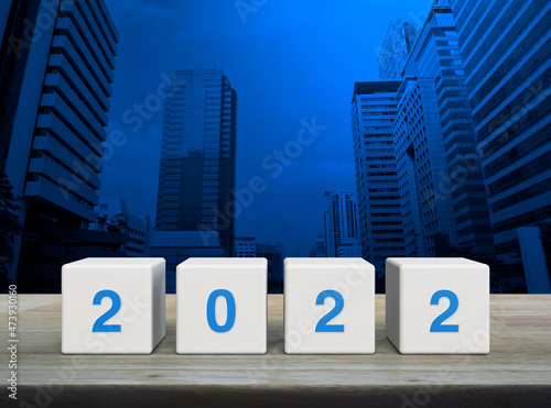 2022 letter on white block cubes on wooden table over modern office city tower and skyscraper, Happy new year 2022 cover concept