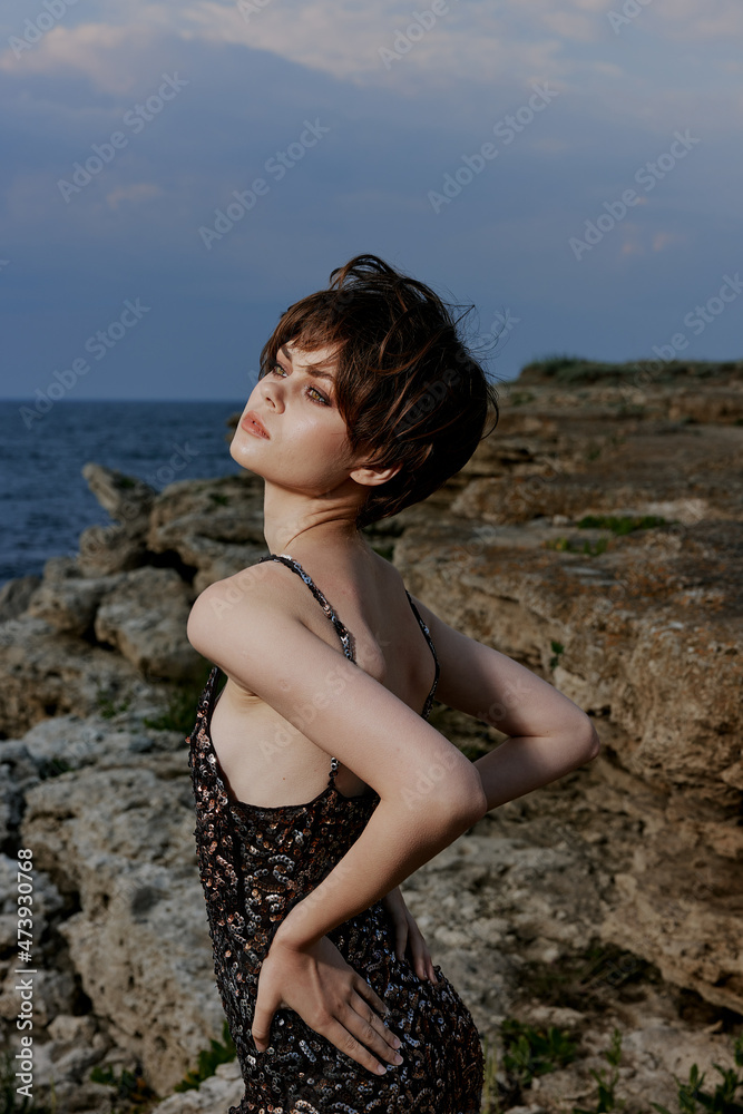 woman with short hair in a shiny dress posing against the backdrop of a rock
