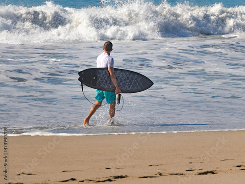 Surfista mirando al horizonte mientras camina en la playa después de tomar algunas olas. 