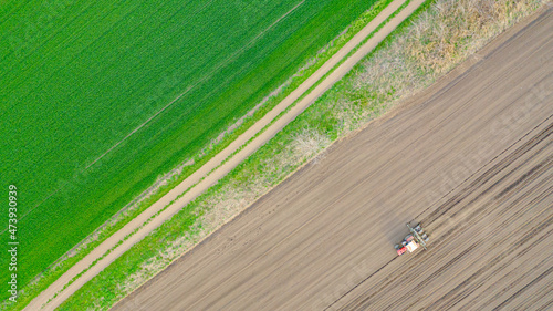 Aerial top view of tractor as dragging a sowing machine over agricultural field, farmland © Roman_23203