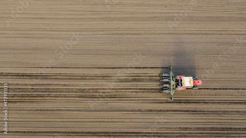 Aerial top view of tractor as dragging a sowing machine over agricultural field, farmland